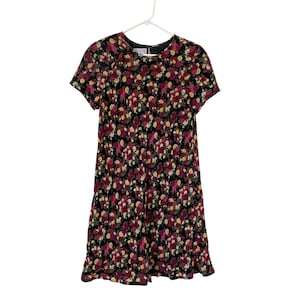 Op de afbeelding: Zwarte jurk met bloemenprint en korte mouwen. De jurk heeft een patroon van rode, gele en witte bloemen. De jurk hangt aan een witte hanger tegen een witte achtergrond.