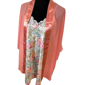 May include: A peach-colored sheer robe with a satin-finish trim worn over a sleeveless nightgown. The nightgown features a floral pattern with pink and white flowers on a light background and a white lace trim along the neckline.