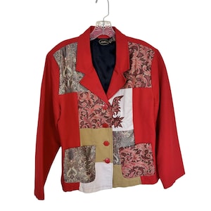 May include: A red blazer featuring a patchwork design with panels of solid red, tan, white, and a dark red and gold floral brocade pattern. The jacket has a notched lapel, a black interior lining, and three red buttons down the front center.