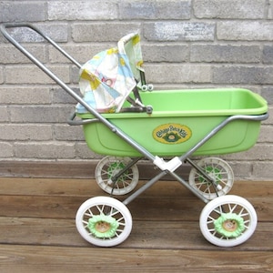 May include: A green Cabbage Patch Kids doll's pram with a white canopy and white wheels with green Cabbage Patch Kids faces on them.