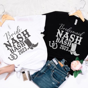 May include: Two white and black t-shirts with a silver glitter design. The white shirt says "Bride Nash Bash 2023" with a horseshoe and a boot. The black shirt says "Bridesmaid Nash Bash 2023" with a horseshoe and a boot.