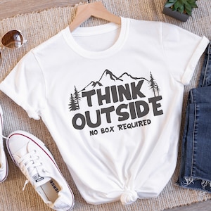 May include: White t-shirt with a black mountain graphic and the text "Think Outside No Box Required".