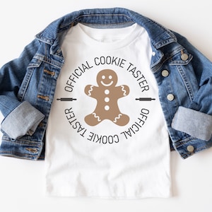 May include: White t-shirt with a brown gingerbread man graphic and the text "Official Cookie Taster" in a circle.