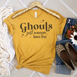 May include: A mustard yellow t-shirt with the text "Ghouls just wanna have fun" in black lettering with small star accents.