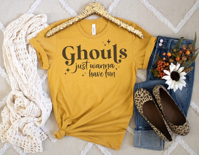 May include: A mustard yellow t-shirt with the text "Ghouls just wanna have fun" in black lettering with small star accents.