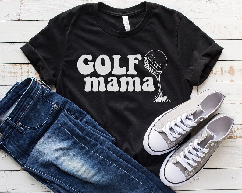 Op de afbeelding: Zwart T-shirt met witte tekst "GOLF mama" en een witte golfbal op een tee.
