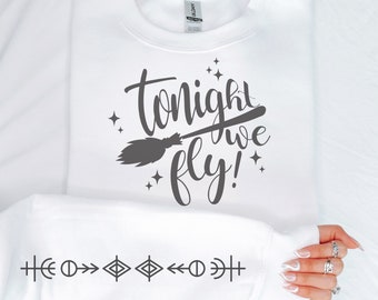 May include: White sweatshirt with the phrase "Tonight we fly!" in dark gray script, accompanied by a broom graphic and stars. The sleeve features a series of geometric symbols. A cozy, casual top for Halloween or witchy themes.