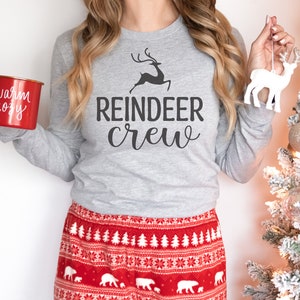 May include: A grey long-sleeved shirt with the text "Reindeer Crew" and a reindeer graphic. The shirt is paired with red and white patterned pyjama trousers.