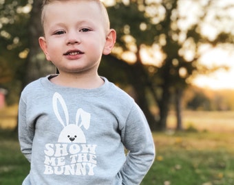 May include: A young child wearing a grey sweatshirt with a white bunny graphic and the text "Show Me The Bunny".