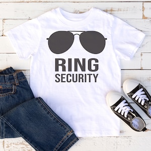 May include: White t-shirt featuring a graphic of sunglasses and the text "RING SECURITY". A pair of blue jeans and black trainers are also in the image.