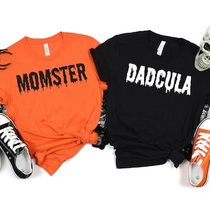 May include: Two Halloween themed t-shirts, one orange with "Momster" in black dripping letters and one black with "Dadcula" in white dripping letters.