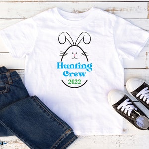May include: White t-shirt with a black and white bunny rabbit inside an egg with the text "Hunting Crew 2022" in blue and green.
