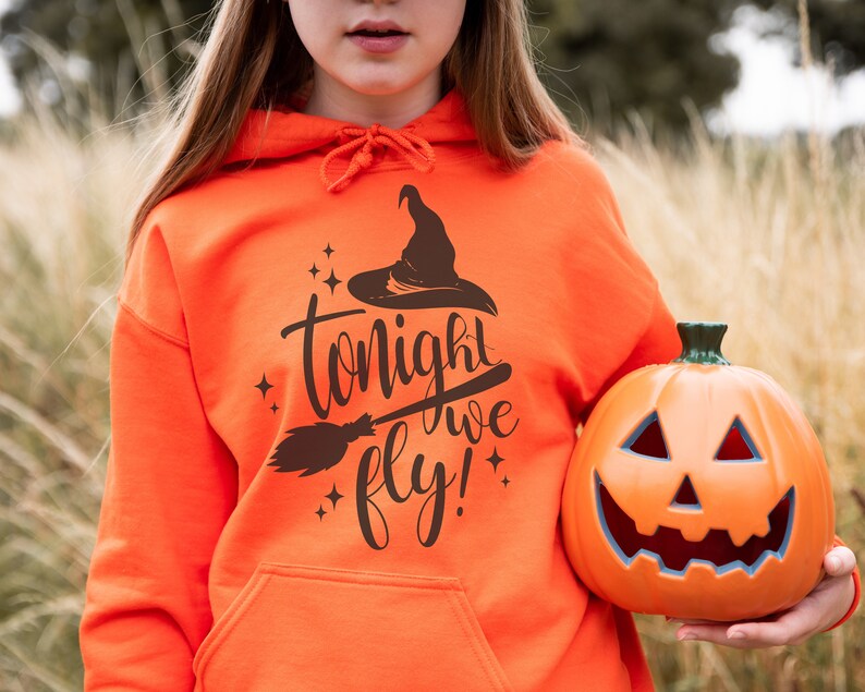 May include: A bright orange hoodie with a black witch hat and broom graphic and the text "tonight we fly!" A person is holding an orange jack-o'-lantern.
