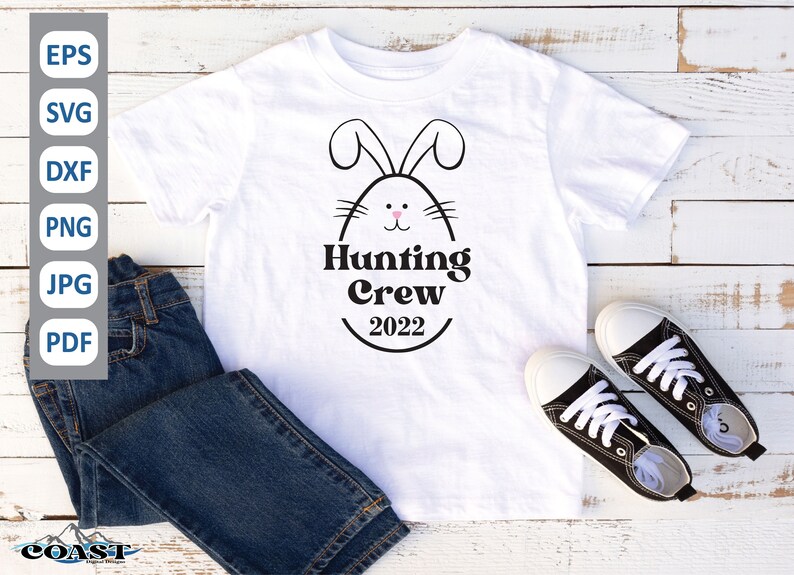May include: White t-shirt with a black bunny silhouette and the text "Hunting Crew 2022". The bunny has pink ears and a pink nose. The t-shirt is on a white wooden surface with blue jeans and black sneakers.