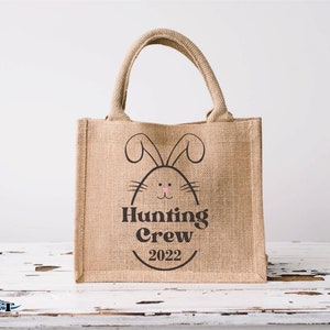 May include: A brown burlap tote bag with a black bunny silhouette and the text "Hunting Crew 2022".