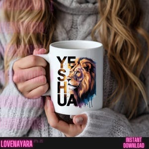 K&ouml;nnte beinhalten: Wei&szlig;e Keramiktasse mit dem Wort "YESHUA" in Gold- und Schwarzt&ouml;nen und einer Illustration eines L&ouml;wenkopfes in Gold-, Braun- und Blaut&ouml;nen. Die Tasse wird von einer Person gehalten, die einen grauen Pullover tr&auml;gt.
