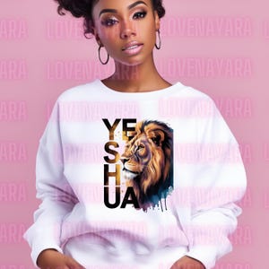K&ouml;nnte beinhalten: Wei&szlig;es Sweatshirt mit einer detaillierten Illustration eines L&ouml;wenkopfes und dem Text "YESHUA" in Schwarz und Gold. Der L&ouml;we hat eine goldene M&auml;hne und einen Aquarell-Hintergrund in Blau und Schwarz.