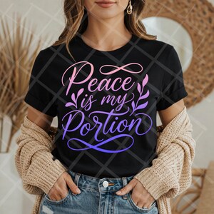 May include: Black t-shirt with the text "Peace is my Portion" in a gradient of pink and purple. The design includes floral accents. The shirt is worn with blue jeans and a beige cardigan.
