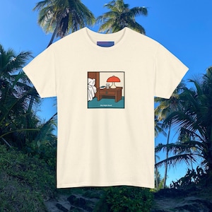Könnte beinhalten: Ein cremefarbenes Kurzarm-T-Shirt mit einer quadratischen Grafik auf der Brust. Die Illustration zeigt einen braunen Nachttisch aus Holz mit einer roten Lampe, einem Buch und einem Becher, wobei der Text "One Night Stand" darunter steht.