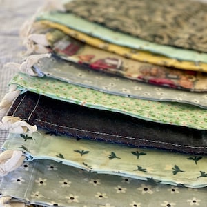 May include: A stack of 10 reusable fabric produce bags with various patterns, including floral, geometric, and bee designs. The bags are made of cotton and have a drawstring closure.