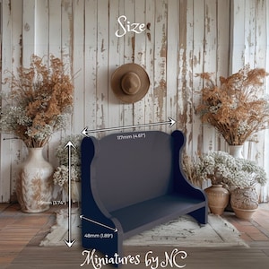 Könnte beinhalten: Eine dunkelblaue, hölzerne Miniaturbank mit Rückenlehne und Armlehnen. Die Bank ist 11,7 cm breit, 4,8 cm hoch und 9,5 cm tief. Die Bank steht auf einem Teppich vor einer weißen Holzwand.