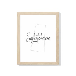 May include: A framed print of a line drawing of the province of Saskatchewan, Canada. The text "Saskatchewan" is written in cursive below the outline of the province.