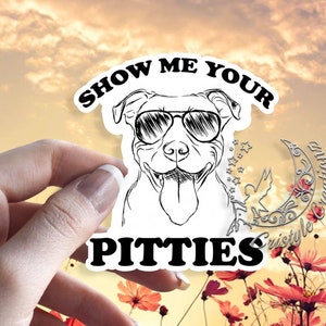 May include: A white sticker with a black outline of a dog wearing sunglasses and the text "SHOW ME YOUR PITTIES" in a black, bold font. The sticker is held in front of a floral background.