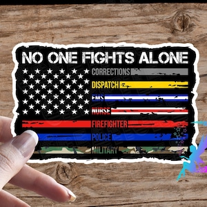 May include: A sticker featuring a distressed American flag design. The flag has thin stripes of red, white, blue, yellow, and grey. The text "No One Fights Alone" is at the top of the sticker. Below the flag are the words "Corrections, Dispatch, EMS, Nurse, Firefighter, Police, Military".
