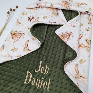 May include: A green minky baby blanket with a white fabric side featuring a Harry Potter themed print. The blanket is personalized with the name "Jeb Daniel" embroidered in a cream color.