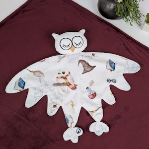 May include: White owl-shaped baby blanket with a white background and a pattern of owls, books, and other Harry Potter-themed imagery. The blanket is soft and cuddly, perfect for a baby or toddler.
