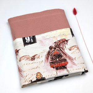 May include: A pink and white fabric with a vintage train design. The train is a steam engine with a red and black color scheme. The fabric has a handwritten text pattern and a sign that reads "9 3/4".