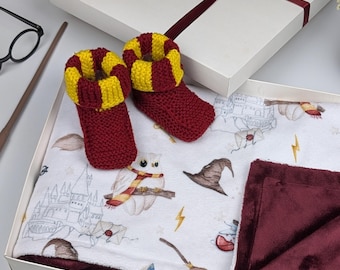 May include: A white baby blanket with a Harry Potter theme featuring owls, lightning bolts, and Hogwarts castle. The blanket is paired with a set of red and yellow knitted baby booties.