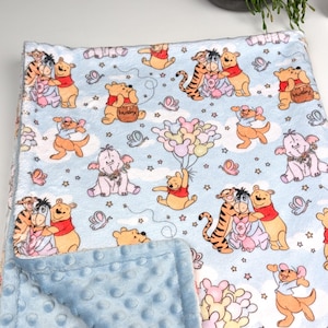 May include: A blue baby blanket featuring a Winnie the Pooh theme. The blanket showcases various Winnie the Pooh characters, such as Winnie the Pooh, Tigger, Piglet, and Eeyore. The blanket is crafted from soft, plush fabric, ideal for snuggling.