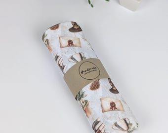 May include: A white baby blanket with a whimsical pattern of books, envelopes, cups, and broomsticks. The blanket is rolled up and tied with a brown paper band that says "Handmade Baby Blankets for Love".