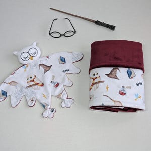 May include: A white owl-shaped security blanket with a burgundy fleece backing. The blanket features a white background with a repeating pattern of owls, glasses, books, and other Harry Potter themed imagery.