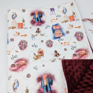 May include: A white and burgundy baby blanket with a Harry Potter theme. The blanket features a repeating pattern of owls, glasses, wands, and other Harry Potter imagery. The back of the blanket is a solid burgundy color.