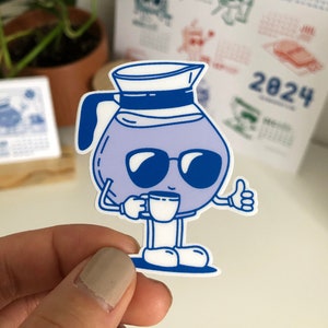 May include: A blue cartoon coffee pot with sunglasses and a white sailor hat is holding a white coffee cup. The coffee pot is smiling and giving a thumbs up. The background is a calendar with the year 2024.
