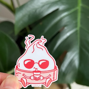Peut inclure: Une illustration de dessin animé rouge et blanc d'une boulette portant des lunettes de soleil et tenant un thé à la boba. La boulette est assise sur un coussin rose avec le texte "studio-lz" en dessous.