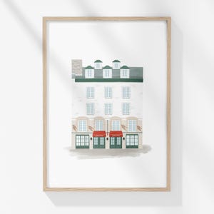 以下が含まれることがあります： 白い建物に緑色の縁取りと赤い日よけが付いたイラストが額装されています。建物には窓がいくつかあり、屋根は緑色です。イラストは白い背景に描かれています。