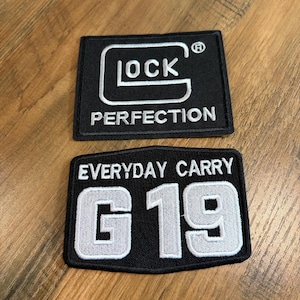 May include: Two rectangular embroidered patches with black backgrounds and white stitching. The top patch features the Glock logo and the word PERFECTION. The bottom patch displays the text EVERYDAY CARRY above the large alphanumeric characters G 19.
