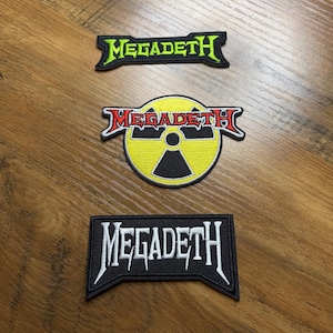 May include: Three embroidered patches with the word "MEGADETH". One patch is green and black, another is red, yellow, and black with a radiation symbol, and the third is black and white.
