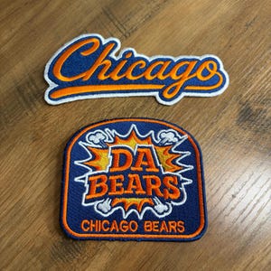 May include: Two embroidered fabric patches. The top patch features the word Chicago in orange script with a blue outline on a white background. The bottom patch is a blue shield shape with orange text reading DA BEARS and CHICAGO BEARS.