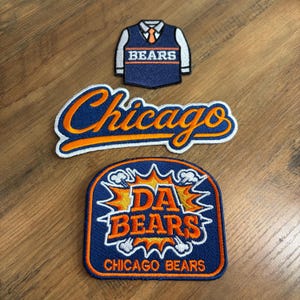 May include: Three embroidered patches featuring Chicago Bears themes. One patch shows a blue sweater vest with a white shirt and orange tie. Another is a script logo reading Chicago in orange and blue. The third is a shield with DA BEARS text.