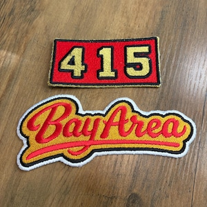 May include: Two embroidered patches. The top rectangular patch is red with a black border and features the gold numbers 415. The bottom patch is shaped with a white border and features the red cursive text Bay Area on a gold background.