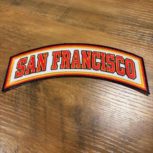 May include: A set of three ceramic mugs with a speckled, cream-colored glaze. Each mug features a different hand-painted floral design in shades of blue, green, and yellow. The mugs have a simple, rounded shape.