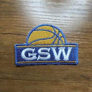 May include: Embroidered patch featuring a basketball design in gold and blue. The patch has the letters "GSW" in white on a blue background. The patch is rectangular with a curved top, suitable for apparel or accessories.