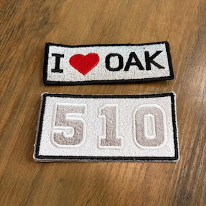 May include: Two rectangular embroidered patches. The top patch features the text I, a red heart symbol, and the word OAK in black on a light gray background with a black border. The bottom patch displays the number 510 in light gray with a black border.