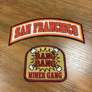 May include: Two embroidered patches. The top patch is arched and reads "SAN FRANCISCO" in red letters with a white border. The bottom patch is rectangular with "BANG BANG" and "NINER GANG" in red letters.