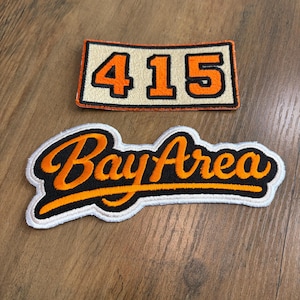 May include: Two embroidered patches. The top rectangular patch features the orange numbers 415 on a cream background with a black border. The bottom patch features the orange script text Bay Area with a black outline and a white border.
