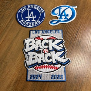 May include: Three embroidered patches featuring the Los Angeles Dodgers logo and text. One patch is circular with the team name, another has a stylized "LA" logo, and the largest reads "Back to Back" with the years 2024 and 2025.